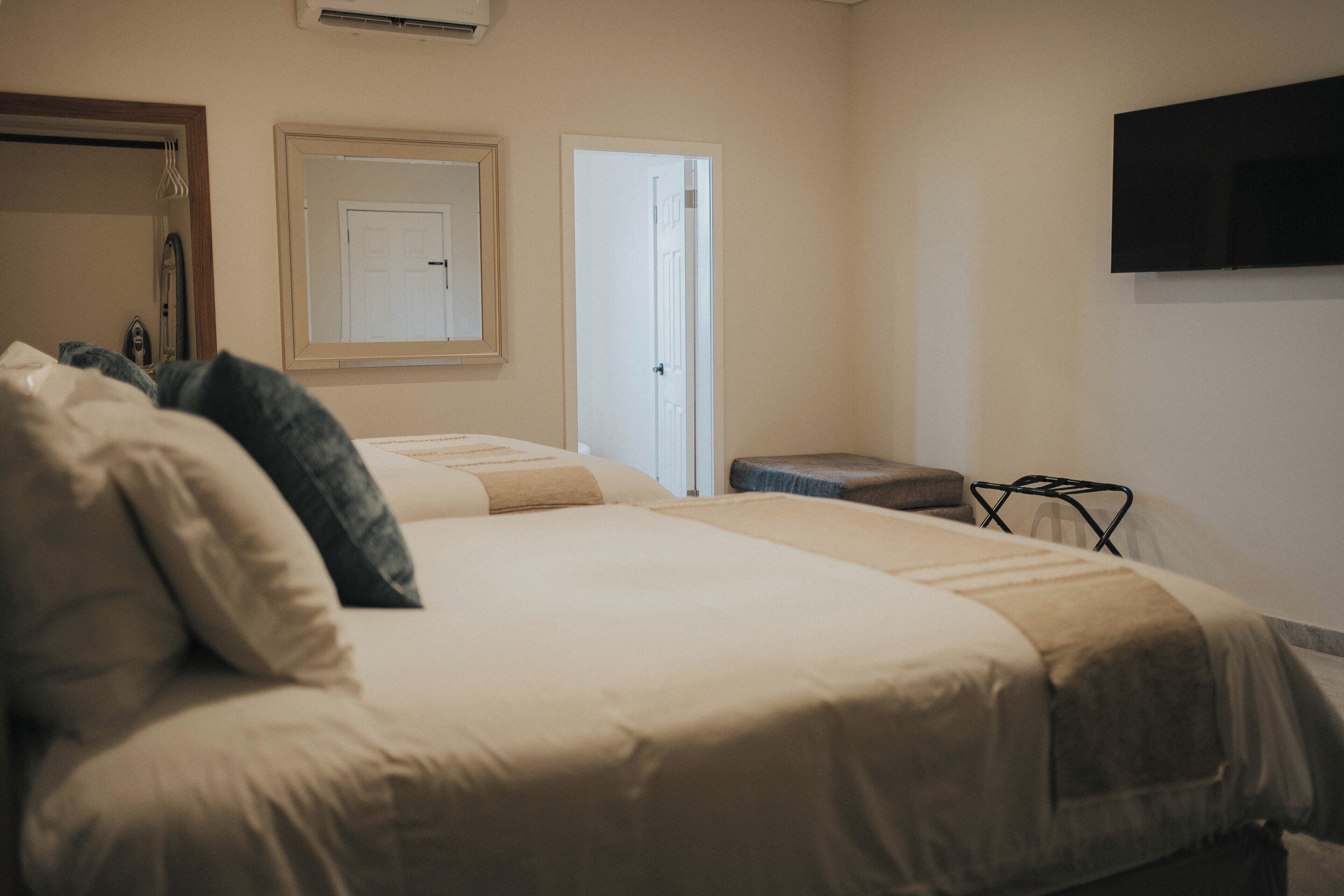 A bedroom with a bed, a bedside table, a mirror, and a TV mounted on the wall.