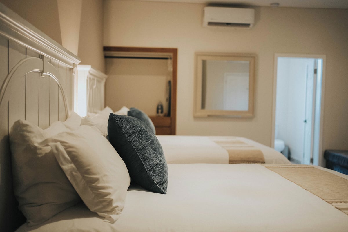 A hotel room with two beds, a wardrobe, a mirror, and an air conditioning unit.