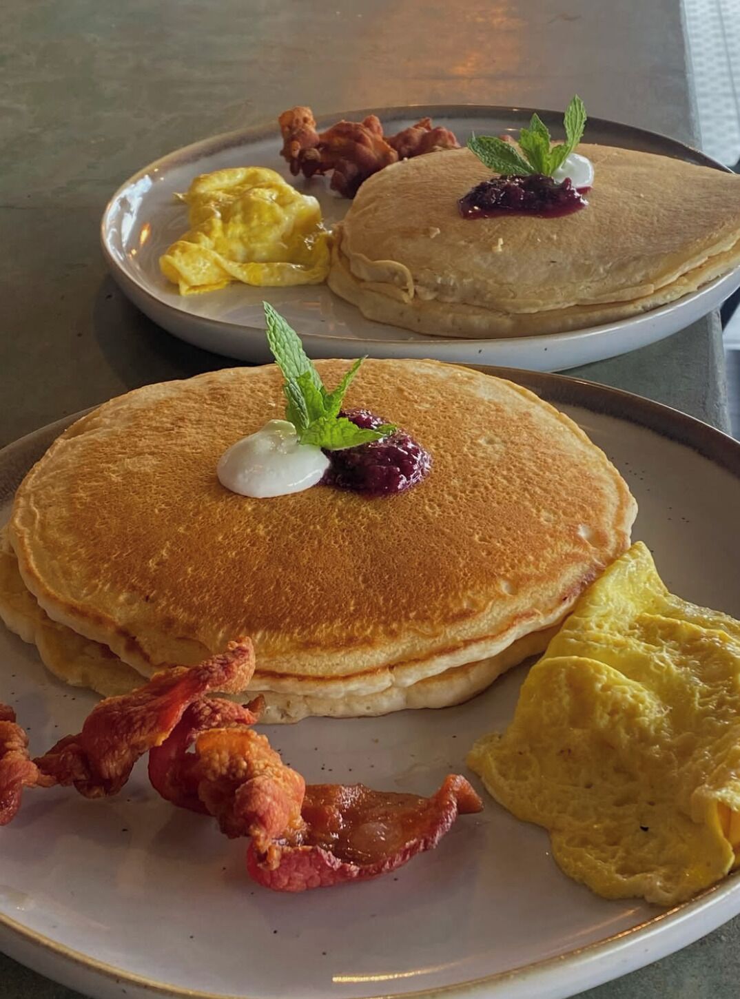 A breakfast plate with pancakes, scrambled eggs, bacon, and a berry compote.