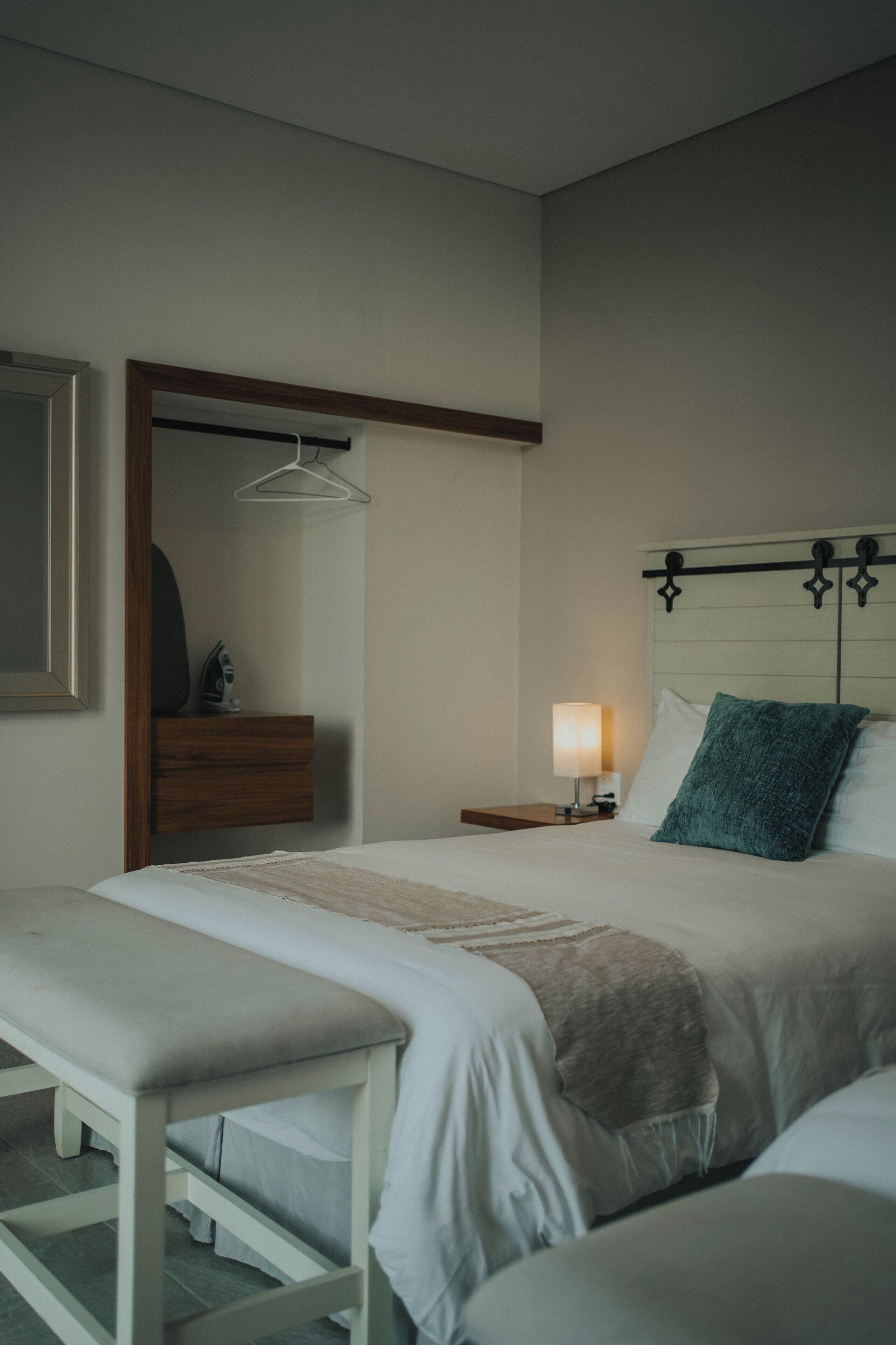 A neatly arranged hotel room with a bed, bedside table, and a bench.