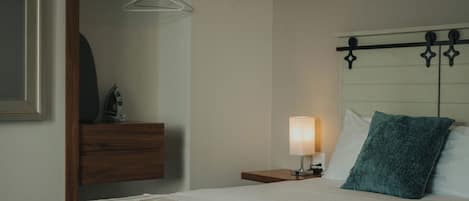 Quarto de hotel bem arrumado, com cama, mesa de cabeceira e um banco.