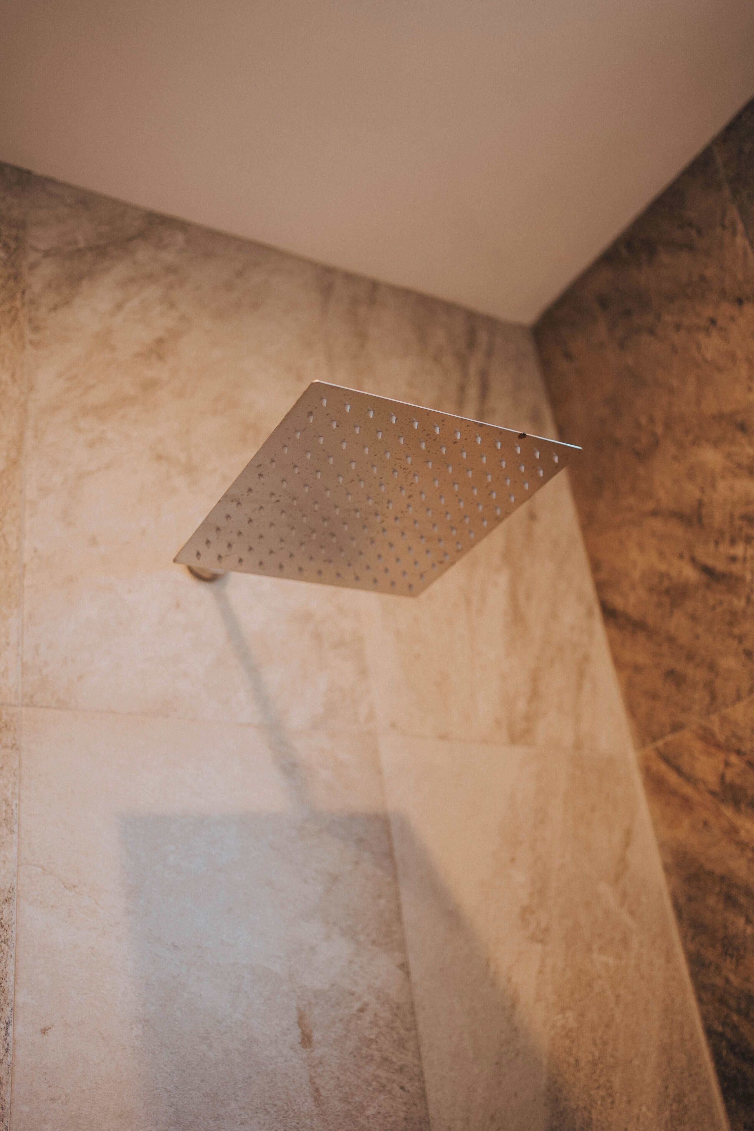 Un pommeau de douche au design perforé, installé sur un mur à texture.