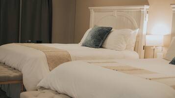 A hotel room with two beds, a bench, and a nightstand with a lamp.