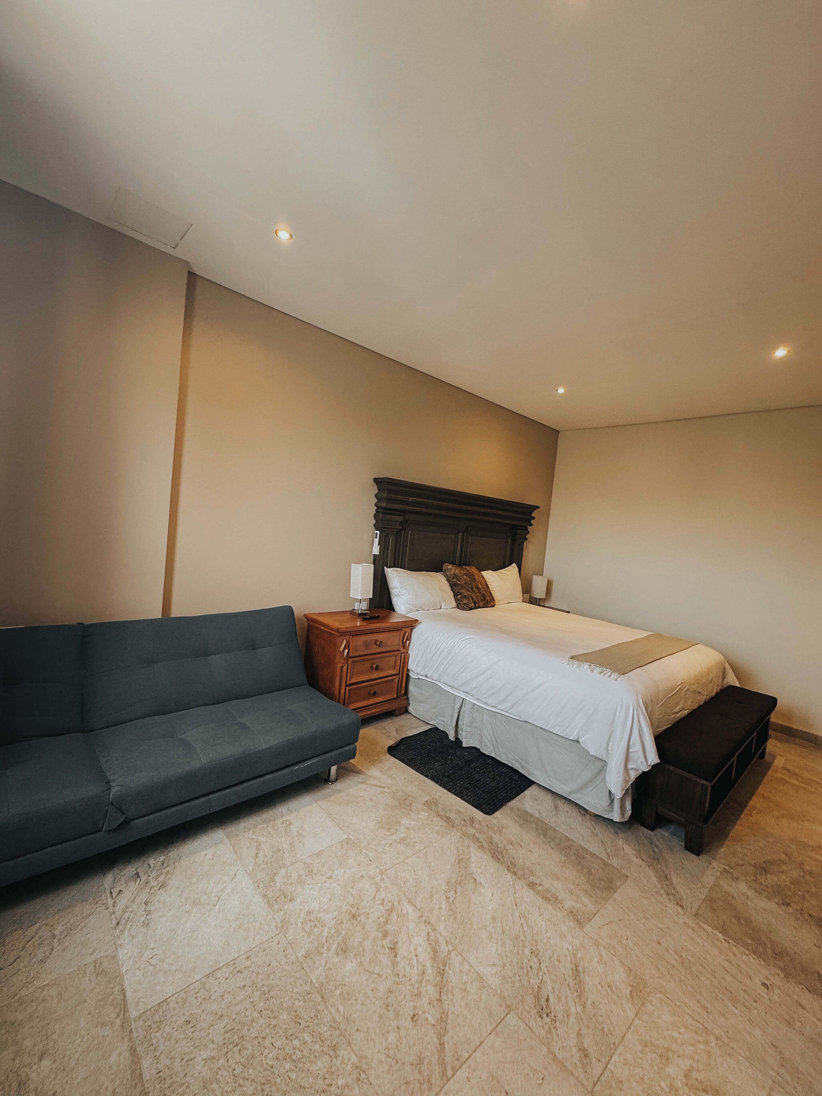 A bedroom with a bed, a nightstand, a sofa, and a bench.