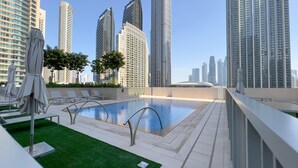 A rooftop pool with lounge chairs and umbrellas, surrounded by high-rise buildings. - HomesGetaway-Luxury 1BRApartment in Forte Downtown (Dubai)