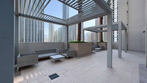 A modern outdoor lounge area with a pergola, seating, and a view of high-rise buildings.