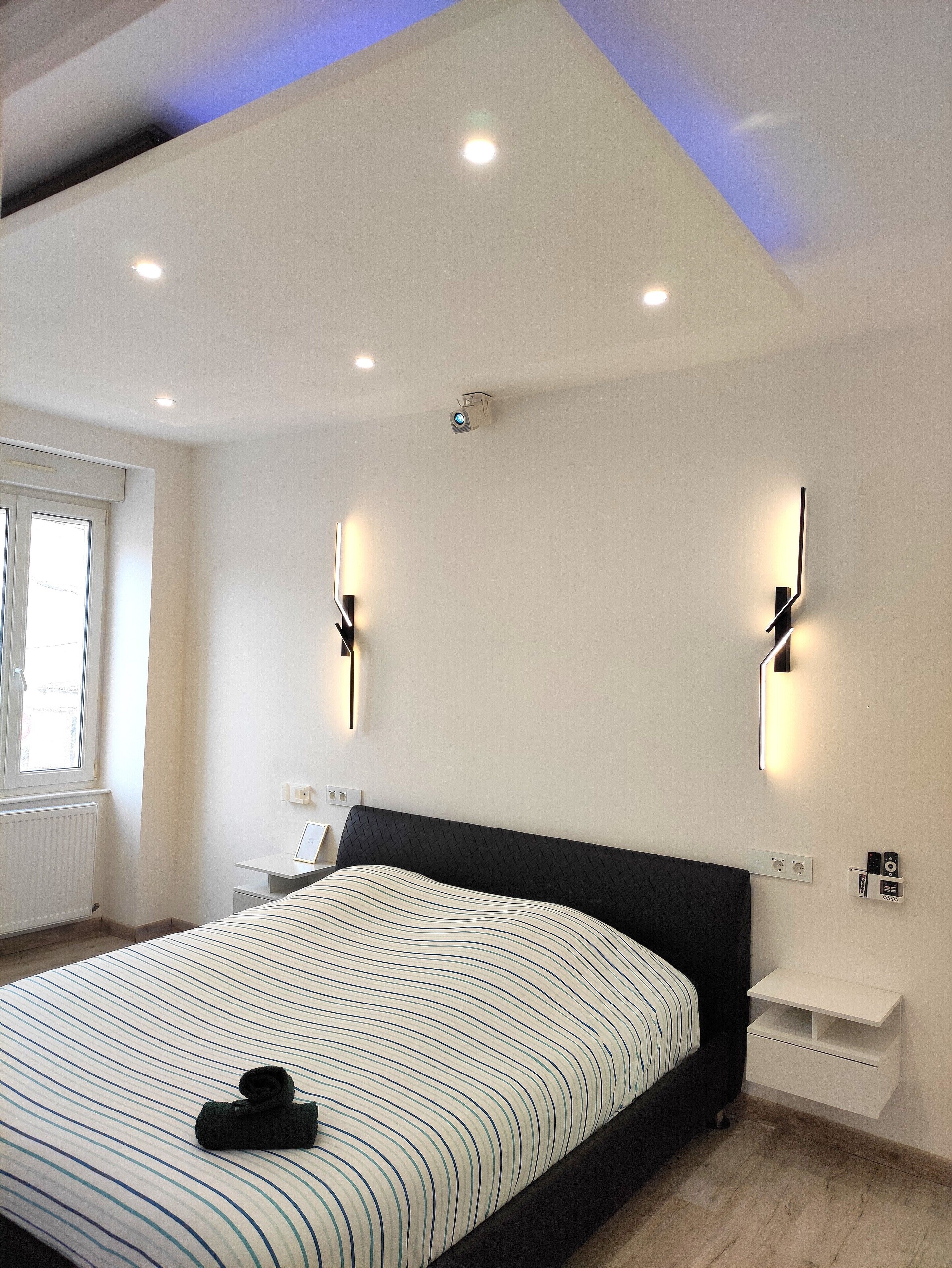 Une chambre moderne dotée d’un grand lit, d’un éclairage encastré au plafond, d’un projecteur et d’appliques murales.