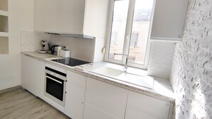 A modern kitchen with white cabinetry, a built-in oven, a sink, and a window with a view of buildings outside. - CinéLux - Private Experience [Full accomodation] [Full accomodation (Algrange)