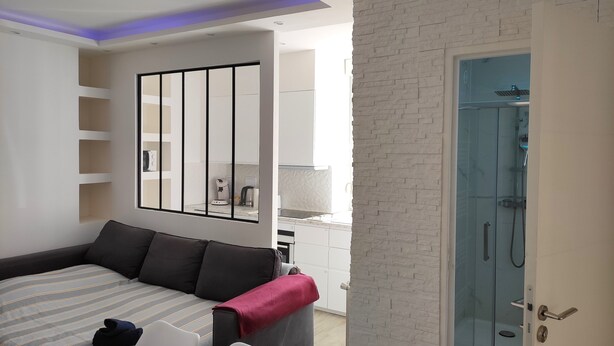 A modern hotel room with a sofa, a dining table, and a glass-enclosed shower area. - CinéLux - Private Experience [Full accomodation] [Full accomodation (Algrange)