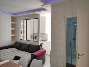 A modern hotel room with a sofa, a dining table, and a glass-enclosed shower area. - CinéLux - Private Experience [Full accomodation] [Full accomodation (Algrange)