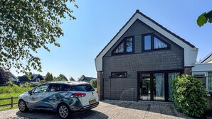Een modern huis met twee verdiepingen, een schuin dak, grote ramen en een oprit van grind.