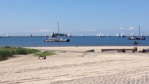 Een strand met boten op het water, een zandvlakte en een verhard pad.