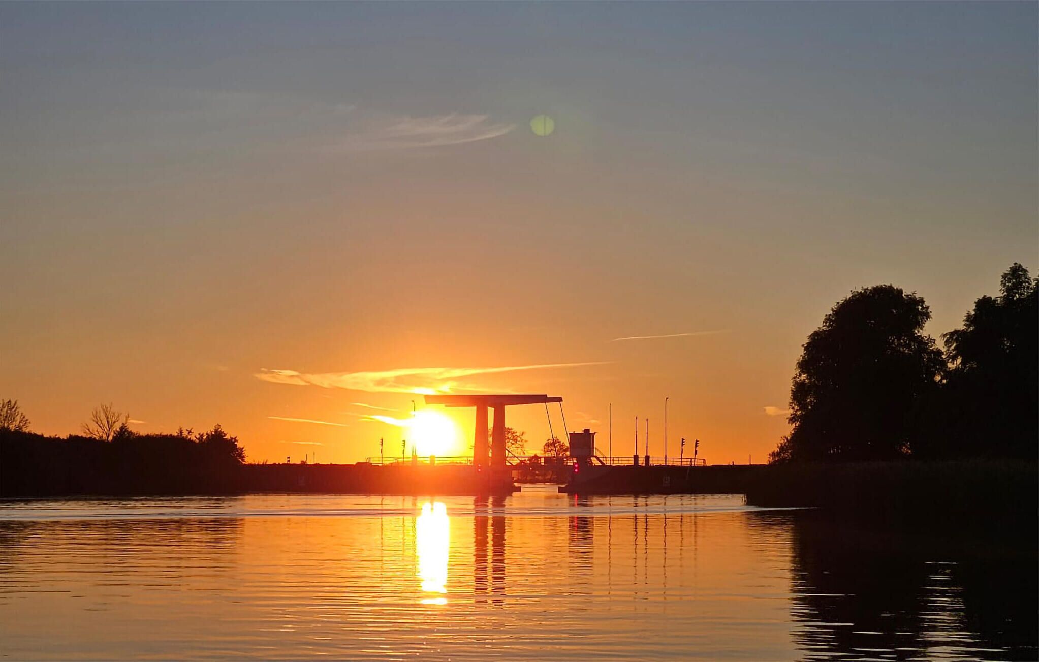 A sunset over a calm body of water with a bridge structure in the foreground.