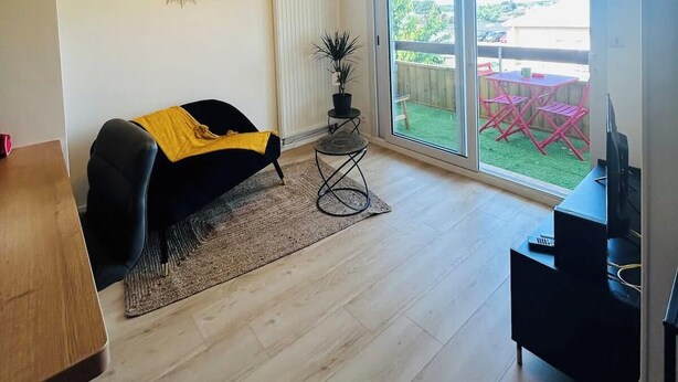 En moderne stue med sofa, sofabord og tv-møbel. Der er en stor skydedør, der fører ud til en baghave med et bord og stole.