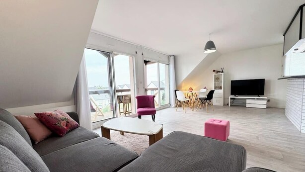 Una sala de estar moderna con un sofá gris, un otoman rosa y un comedor con mesa y sillas.