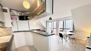 Una cocina moderna con una isla integrada, un comedor con mesa redonda y sillas, y vistas al exterior a través de amplias ventanas.