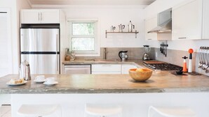 Uma cozinha moderna com armários brancos, geladeira de aço inoxidável, espaço para café e uma ilha de madeira com banquetas.