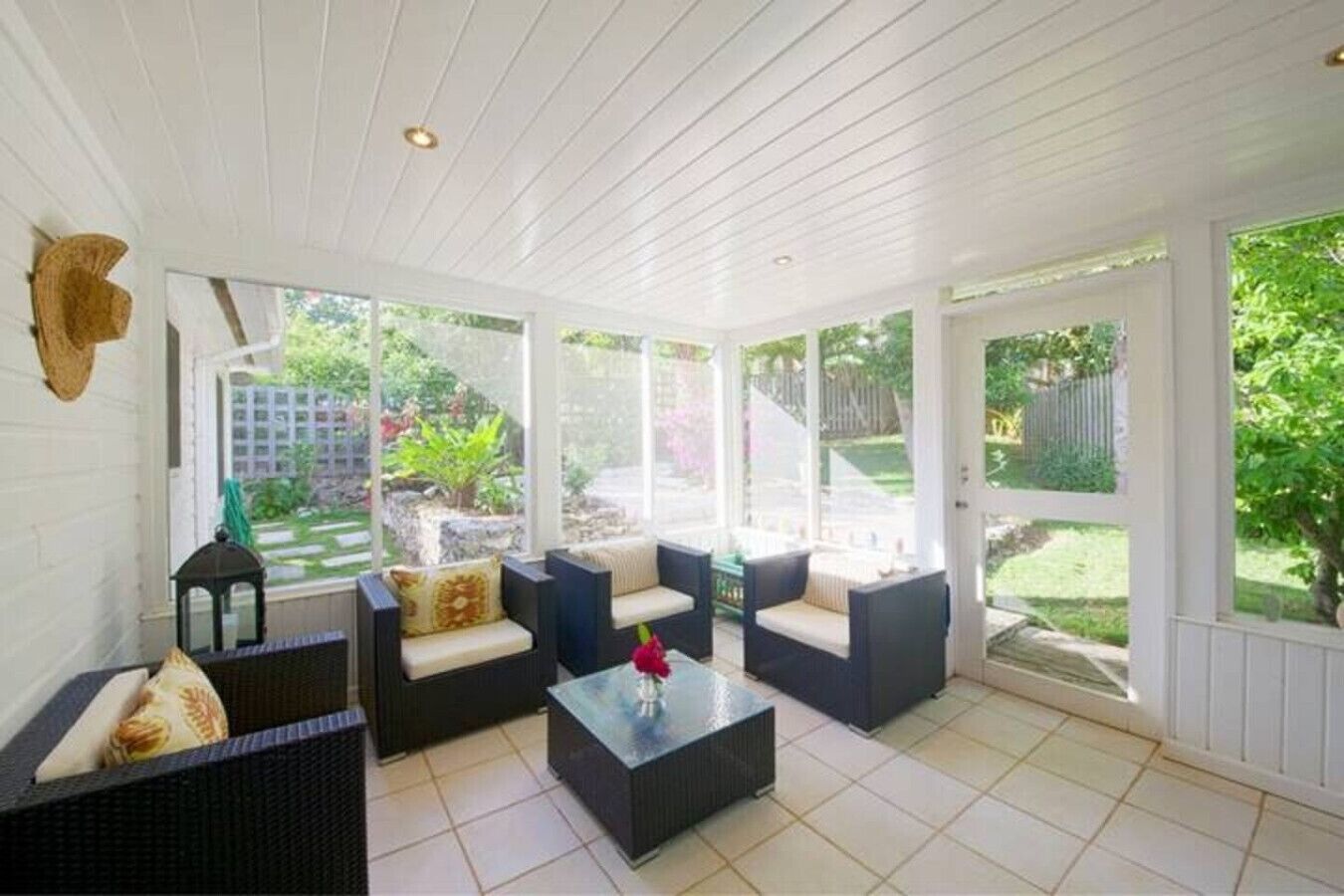 Une terrasse couverte, aménagée avec des meubles en osier, une table basse en verre et offrant une vue sur un jardin.