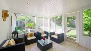 Eira coberta com móveis de vime, mesa de centro de vidro e vista para um jardim.