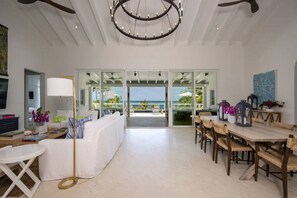 Een ruime woonkamer met uitzicht op de oceaan, een eetgedeelte met rieten stoelen en een moderne kroonluchter.