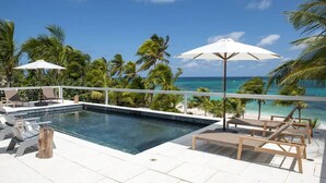Un espace aménagé au bord de la piscine, avec des chaises longues, des parasols et une vue sur l’océan.