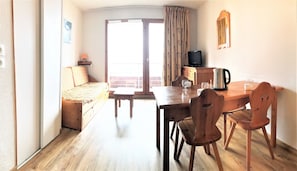 A room with a sofa, a table with chairs, a television, and a window with curtains.