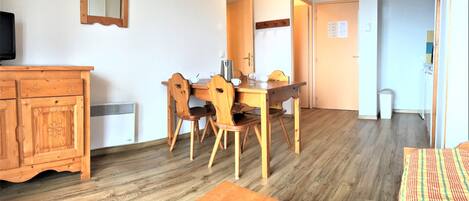 A room with a wooden dining table, chairs, a wooden cabinet, and a mirror on the wall.
