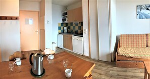 A compact living space with a wooden dining table, a sofa, a kitchenette with a microwave, and a painting on the wall.