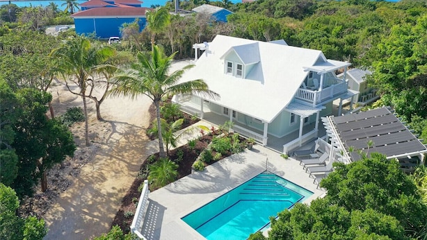A large house with a pool, surrounded by lush greenery and a view of the ocean. - Charming 2BR Island Cottage with Pool & Generator (Governor`s Harbour)