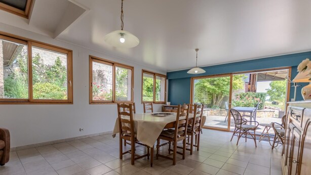 A spacious dining area with a large table and chairs, large windows with a view of greenery, and a ceiling fan. - Le Pétillant - LE BREUIL (LE BREUIL)