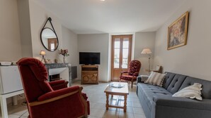 A living room with a sofa, red armchair, TV, and a fireplace. - Le Pétillant - LE BREUIL (LE BREUIL)