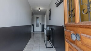 A hallway with a wooden door on the right, a black console table with a vase, and a tiled floor. - Le Pétillant - LE BREUIL (LE BREUIL)
