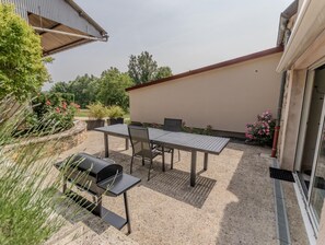 An outdoor patio with a table and chairs, a grill, and potted plants.