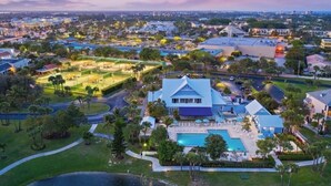 Un hotel grande y moderno con piscina, canchas de tenis y césped bien cuidado.