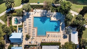 Vista aérea de un resort con una amplia piscina central, sillas de sol y palmeras.