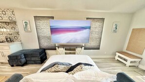 Een moderne slaapkamer met een bed, een televisie, een bankje en een muur met kunstwerken.