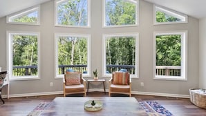 Amplia habitación con ventanas grandes, una mesa de centro de madera, dos sillas y un tapete estampado.