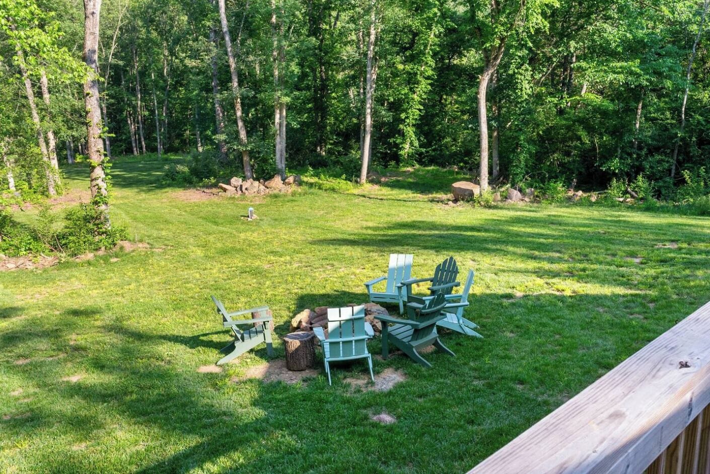 A deck area with Adirondack chairs and a small table, surrounded by a grassy yard and trees.