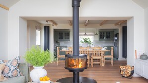 A modern living room with a central fireplace, a dining area, and a kitchen with green cabinets.