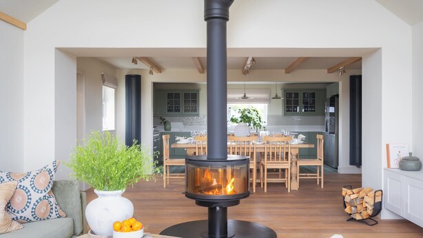 A modern living room with a central fireplace, a dining area, and a kitchen with green cabinets. - Dreamy 5-Bedroom Cottage with Private Hot Tub (Aberyswyth)
