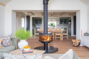 Una sala de estar moderna con chimenea central, comedor y cocina con gabinetes verdes.