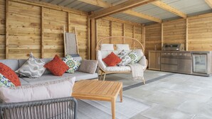 A cozy wooden cabin interior with a sofa, two chairs, a small table, and a kitchenette.