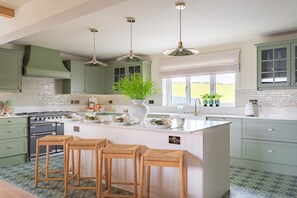 Una cocina con gabinetes verdes, una isla blanca con taburetes, una estufa y un ventanal con vistas al exterior.