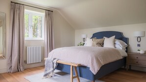 A bedroom with a bed, bedside tables, a bench, a window, curtains, and a radiator. - Dreamy 5-Bedroom Cottage with Private Hot Tub (Aberyswyth)