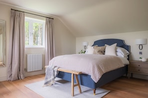 A bedroom with a bed, bedside tables, a bench, a window, curtains, and a radiator.