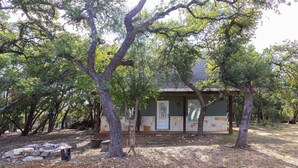 Un chalet rustique entouré d’arbres, avec un foyer en pierre et un banc à proximité.