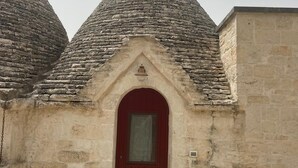 A stone building with a red door, a small porch, and a potted plant.