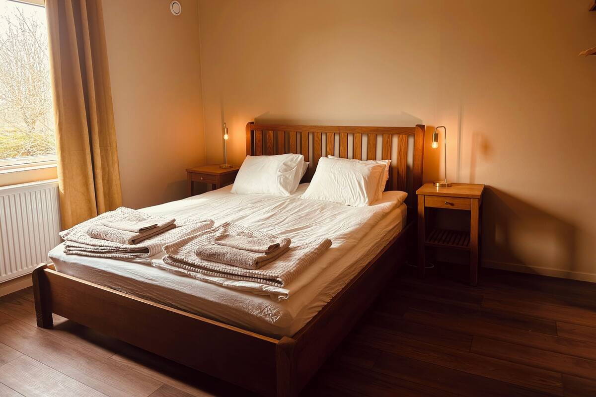 A neatly made bed with a wooden headboard, two bedside tables, and a window with curtains.