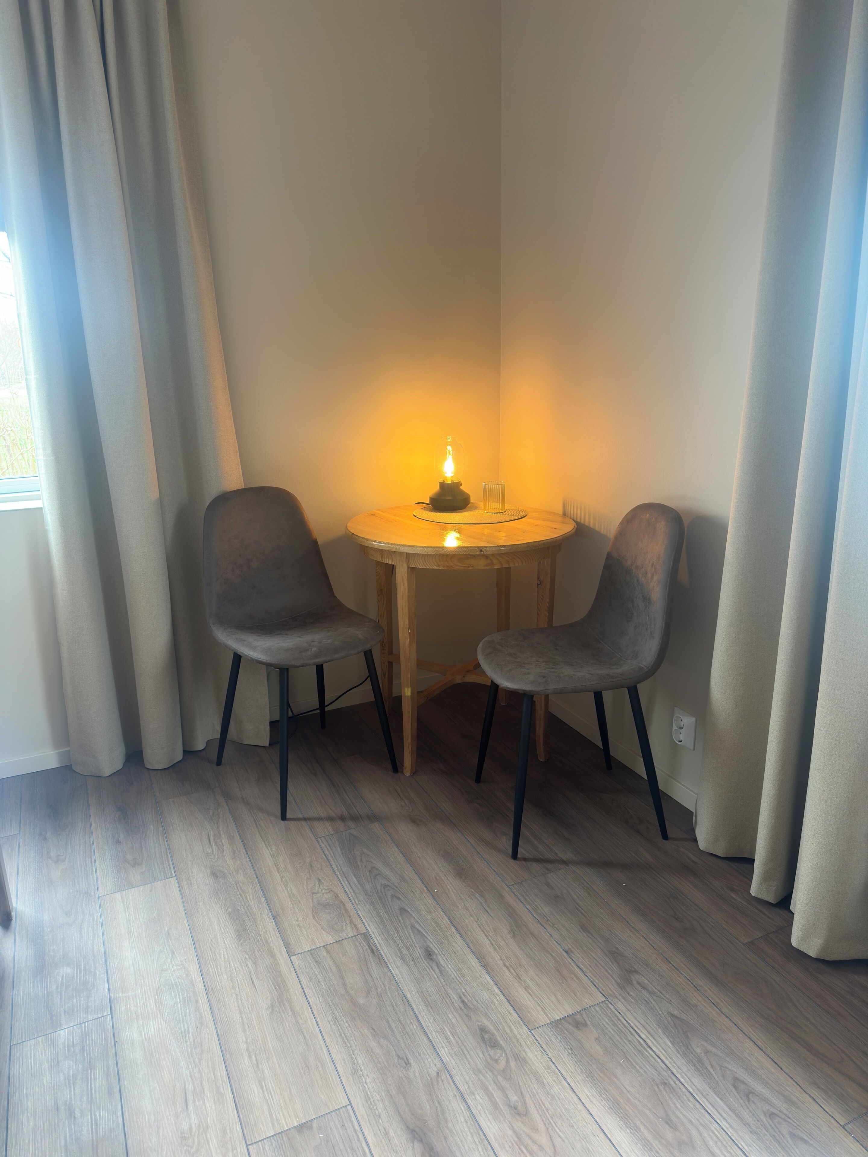 A corner room with two grey chairs, a small round wooden table, and a lit candle.