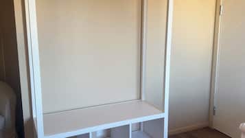 Ett vitt garderobsskåp med en klädstång och hyllor, trägolv och en beige vägg.